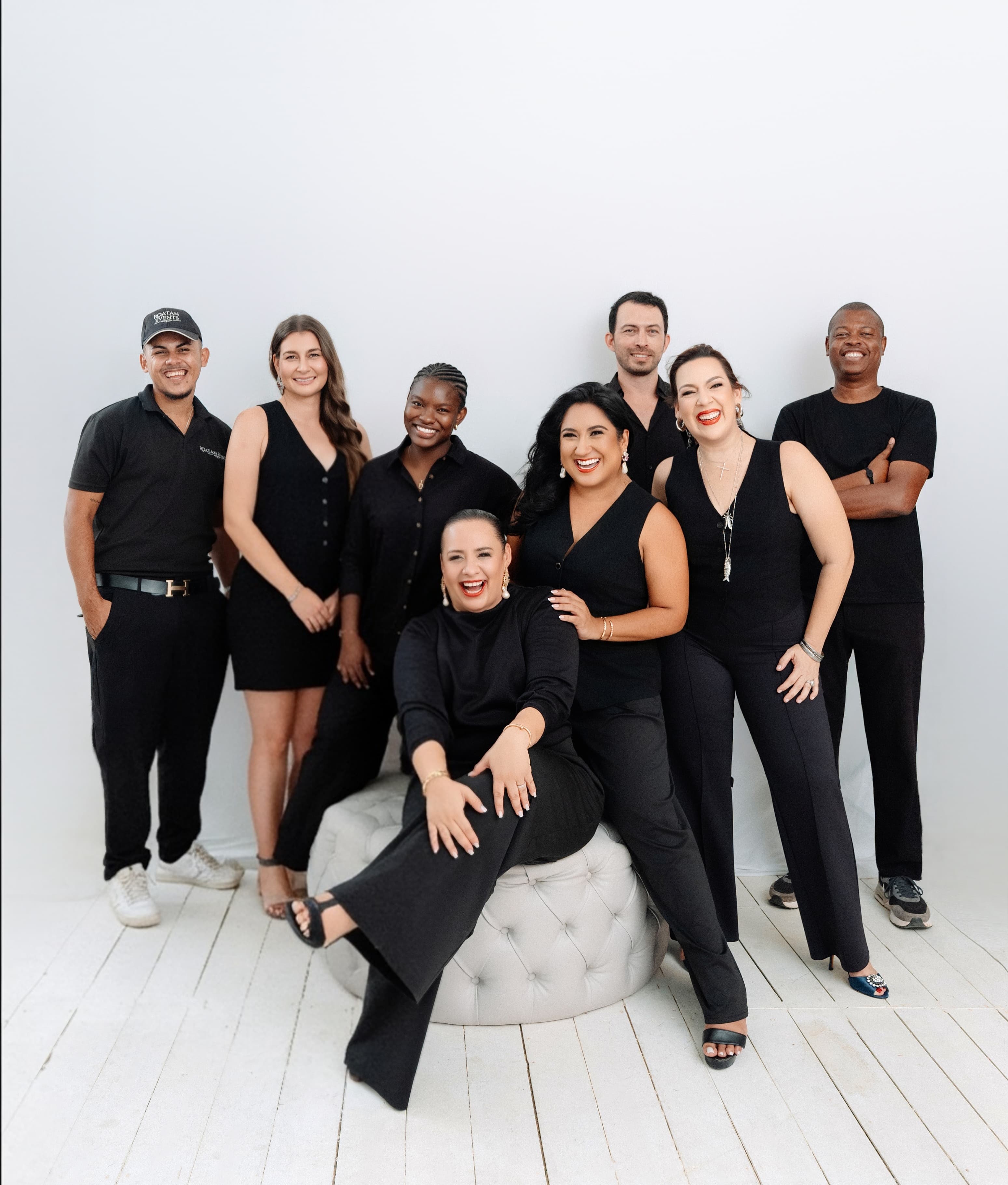 Nine Roatán DMC team members in black attire smiling together in a bright studio portrait
